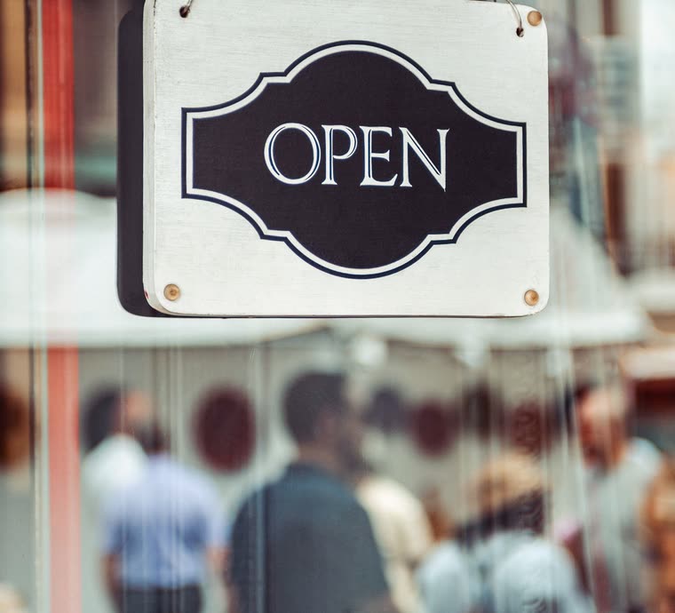 An open sign hanging in a shop window, with people blurred behind the glass