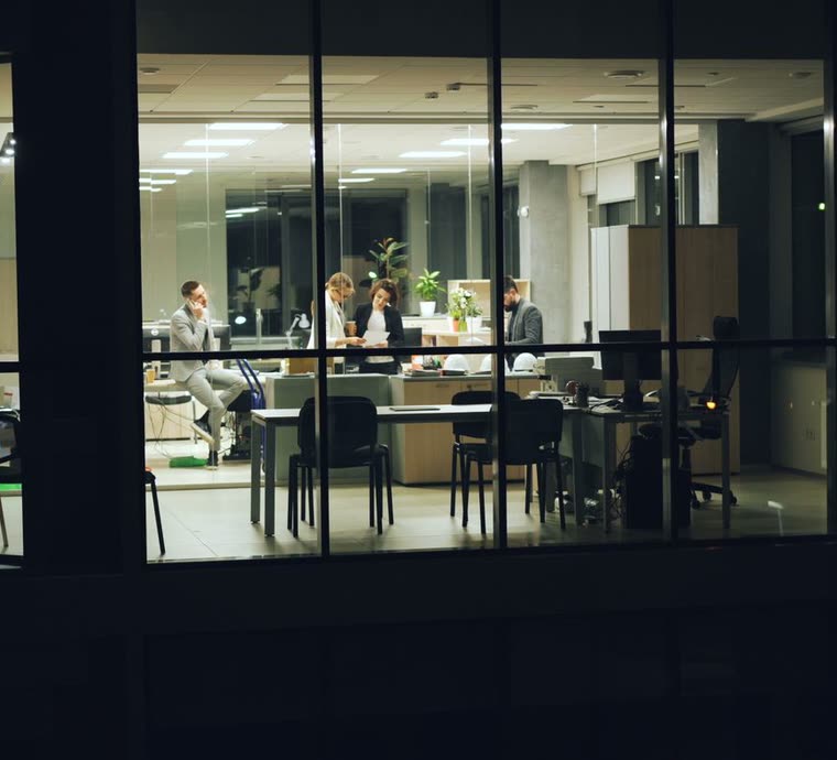 A small office lit up at night, seen from the street through its window